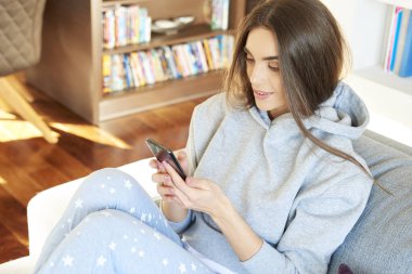 Yüksek açı çekim hoodie ve metin mesajlaşma koltukta evde dinlenirken giyen güzel genç kadın. 