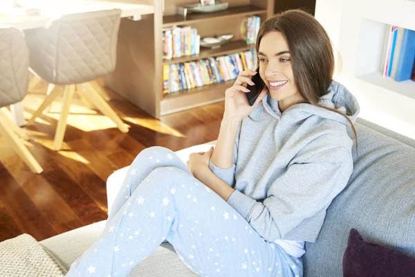 High angle shot of beautiful young woman wearing hoodie and talking with somebody on her cell phone while relaxing on sofa at home.