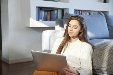 Kanepe evde otururken onu laptop kullanan güzel genç kadın portresi. Ev ofis.