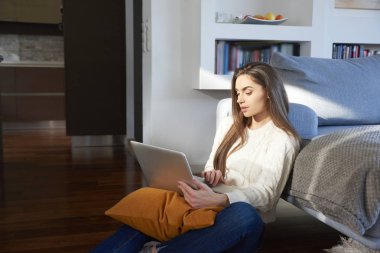 Kanepe evde otururken onu laptop kullanan güzel genç kadın portresi. Ev ofis.