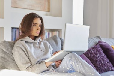 Atış süre kanepede rahatlatıcı ve onu laptop kullanarak hoodie ve pijama pantolon giyiyor rahat bir genç kadının.