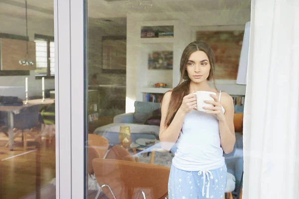 ウィンドウの背後にあるコーヒー カップの側に立って 夢ながらパジャマを着てきれいな若い女性の肖像画 — ストック写真