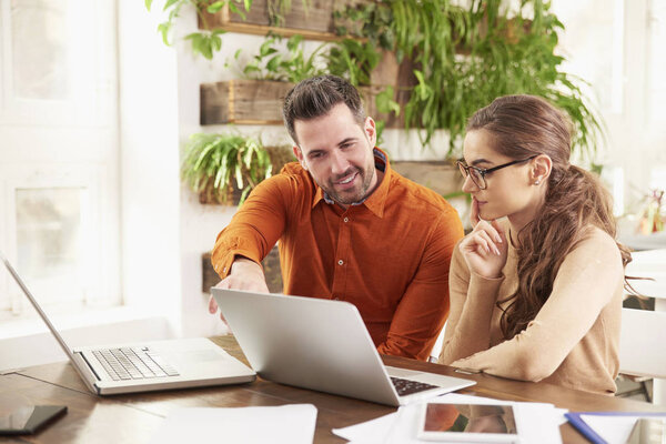 Shot of business people working together in the office. Beautiful young businesswoman sitting in front of laptop wtih his colleague and consulting about business. Teamwork.