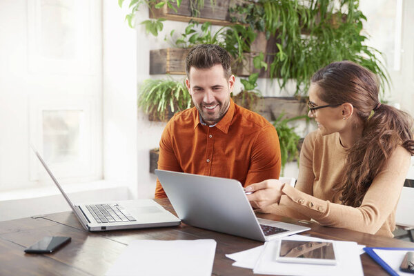 Shot of business people working together in the office. Beautiful young businesswoman sitting in front of laptop wtih his colleague and consulting about business. Teamwork.