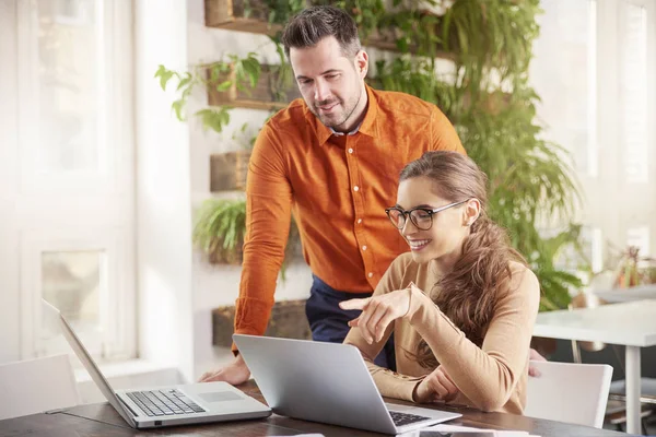 オフィスで一緒に働くビジネスマンのショット 彼女の隣に立って コンサルティング ビジネスについて彼の同僚間のノート パソコンの前に座っている美しい若い実業家 チームワーク — ストック写真