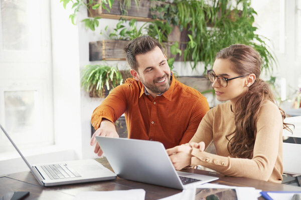 Shot of business people working together in the office. Beautiful young businesswoman sitting in front of laptop wtih his colleague and consulting about business. Teamwork.