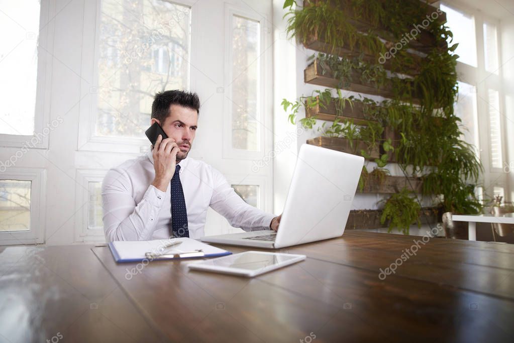 Financial assistant businessman talking on his mobile phone and working on laptop in the office.