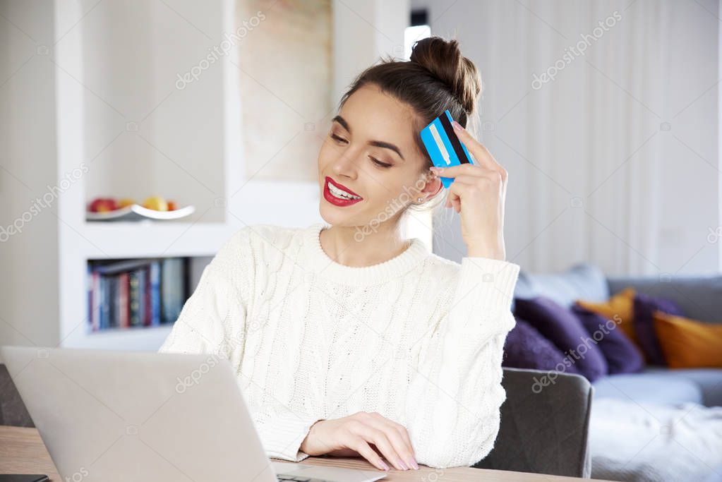 Shot of woman holding her bank card in her hand and using laptop while shopping online at home. 