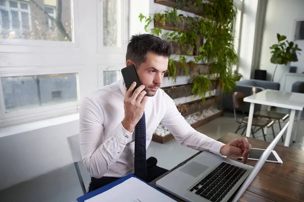 Thinkin financial assistant businessman talking on his mobile phone and working on laptop in the office.