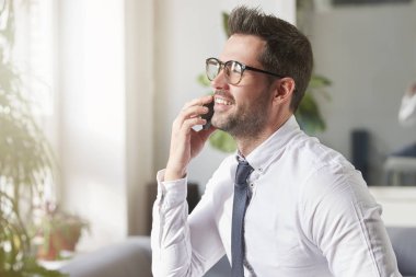 Yakın çekim portre gömlek giymiş yakışıklı işadamı vurdu ve ofiste oturan ve biri ile cep telefonundan konuşuyor süre kravat. 