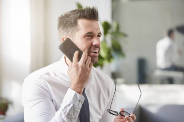 Yakın çekim portre gömlek giymiş yakışıklı işadamı vurdu ve ofiste oturan ve biri ile cep telefonundan konuşuyor süre kravat.