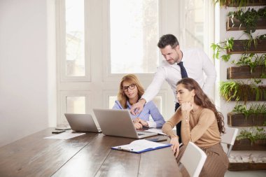 İş adamları iş proje üzerinde birlikte çalışma grubu. Genç satış işkadını ve onların arkasında duran ve tavsiyede mali danışmanı işadamı iken laptop önünde oturan çift olgun profesyonel kadın.