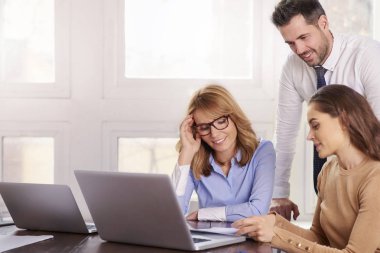 İş adamları iş proje üzerinde birlikte çalışma grubu. Genç satış işkadını ve onların arkasında duran ve tavsiyede mali danışmanı işadamı iken laptop önünde oturan çift olgun profesyonel kadın.