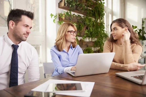 Teamwork in the office. Young secretary and executive financial businesswoman sitting at office desk with their colleague in front of laptop and working toghether on business plan.