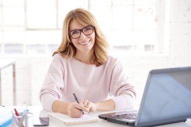 Onu laptop önünde oturan ve bir şey ofiste çalışırken yazma işkadını yakın çekim portre çekici orta yaşlı. 