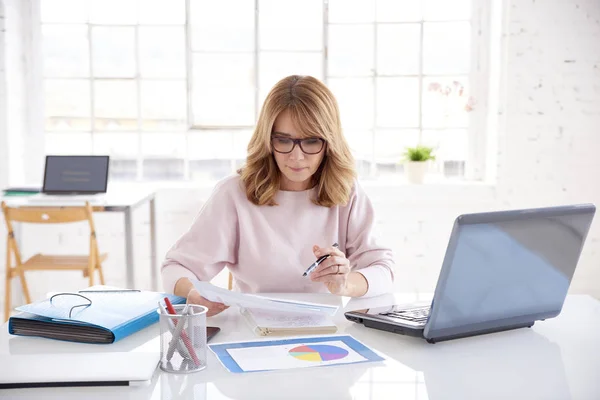 Portrait of financial consultant professional woman doing some paperwork while sitting at office desk and working on laptop.