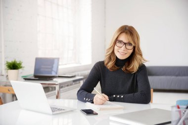 Ofis Masası oturma ve bazı evrak işlerini yaparken rahat kıyafetler giymiş orta yaşlı işkadını, yakın çekim portre vurdu.