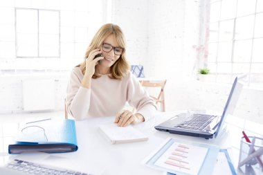 Orta portre çekim biriyle, ofis büro dizüstü bilgisayar ve çalışma önünde otururken cep telefonu konuşurken rahat iş kadını yaşlı. 