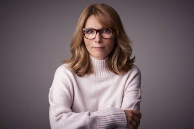 Yakın çekim studio kameraya bakarak ve açık gri renkli otururken gülümseyen orta yaşlı kadın portresi.