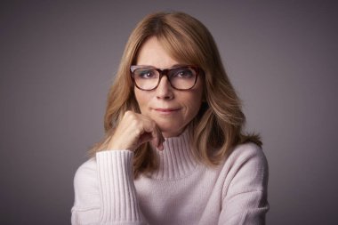 Yakın çekim studio kameraya bakarak ve açık gri renkli otururken gülümseyen orta yaşlı kadın portresi.
