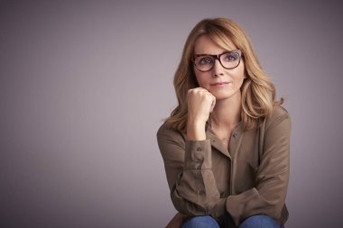 Kameraya bakarak ve gülümseyen açık gri renkli önünde oturan kendine güvenen orta yaşlı kadın portresi stüdyo. 