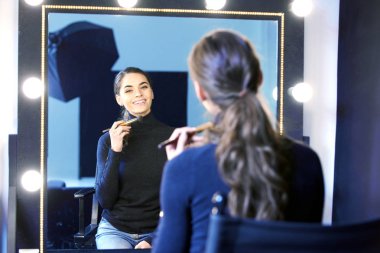 Photostudio aynada, otururken ona makyaj uygulayarak güzel genç kadın portresi.
