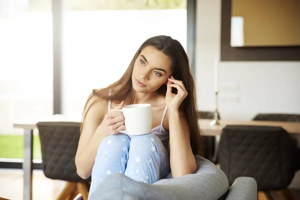 パジャマを着て 自宅のソファでリラックスしながら彼女の朝のお茶を飲む若い女性の肖像画のショット — ストック写真