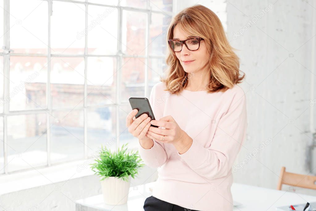 Portrait shot of beautiful middle aged businesswoman text messaging while sitting at desk in the office. 