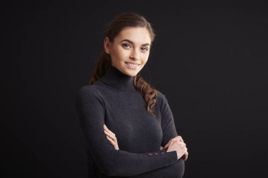 Yakın çekim stüdyo portre çekim giyen güzel genç kadın boyun kazak rulo ve kamera duran kolları olan bakarak geçti koyu arka plan. 