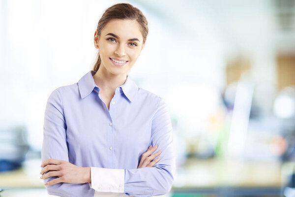 Portrait shot of beautiful businesswoman wearing shirt while standing with arms crossed in the office. 