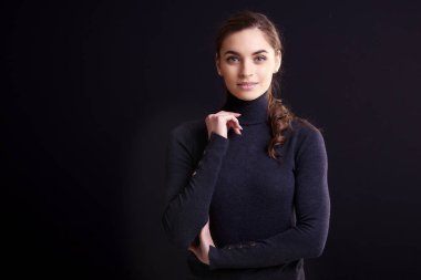 Süre ayakta izole siyah arka plan ve kameraya bakarak boyun kazak giyen güzel genç kadın portre çekim rulo. 