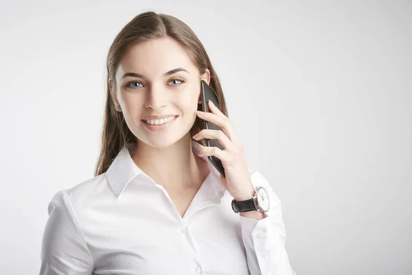 微笑的年轻女商人使用她的手机 并与某人交谈 而站在孤立的白色背景的肖像 — 图库照片