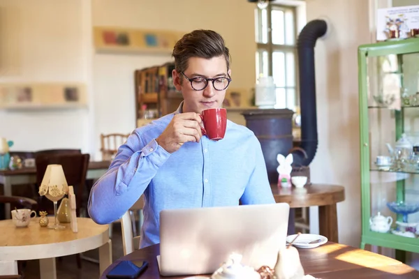 年轻人坐在办公桌前喝咖啡 在小咖啡馆里使用笔记本电脑的肖像照片 小型企业 — 图库照片