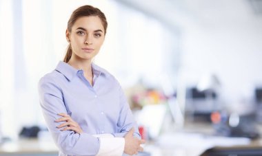 Ofiste kolları katlanmış güzel genç iş kadını. Kameraya bakarken ve gülümserken gömlek giyen gülümseyen profesyonel kadın.