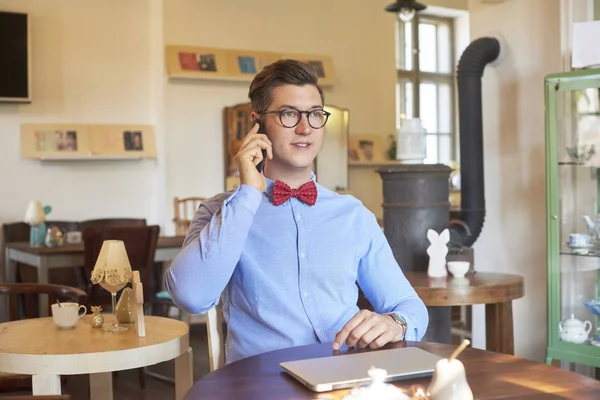 一个英俊的年轻人坐在一个小咖啡馆的办公桌前 打电话的镜头 小型企业 — 图库照片