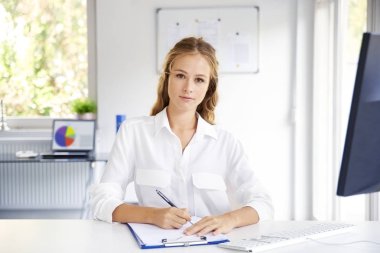 Güzel genç kadın, ofis masası bilgisayar ve çalışma önünde otururken notlar yapma. 