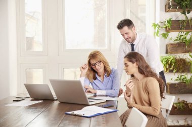 İş adamları iş proje üzerinde birlikte çalışma grubu. Genç satış işkadını ve onların arkasında duran ve tavsiyede mali danışmanı işadamı iken laptop önünde oturan çift olgun profesyonel kadın.