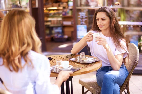 机に座ってコーヒーとクロワッサンを食べながらカフェで話している女性の友人のショット — ストック写真