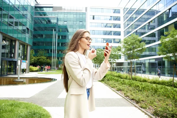 Junge Frau trägt Lippenstift auf, während sie auf der Straße steht — Stockfoto