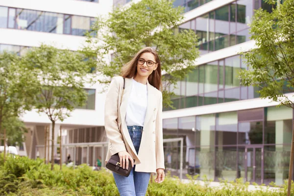Usmívající se mladá žena chůze po ulici poblíž kanceláře bu — Stock fotografie
