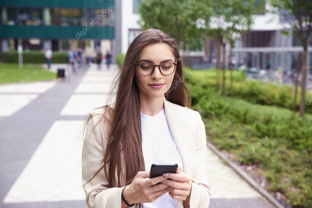 Shot of young businesswoman text messaging while walking on the street. 