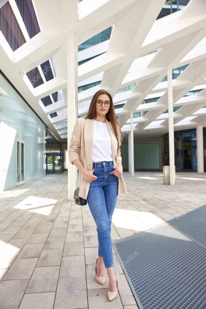 Full length shot of young businesswoman wearing blazer and jeans while walking on the street.