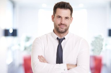 Portrait shot of smiling businessman wearing shirt and tie while standing in the office and smiling.  clipart