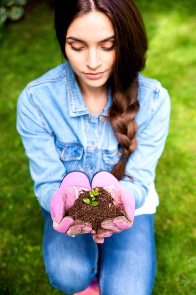 手に土から成長する植物を持ちながら手袋をしている美しい若い女性のクローズアップショット — ストック写真