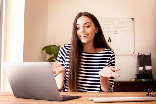 Shot of happy businesswoman talking to her colleagues about business plan in video conference while sitting behind her laptop at home. Home office.
