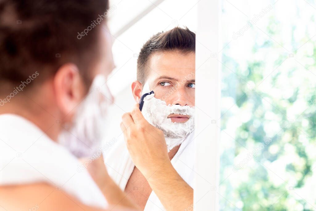 Cropped shot of a man with towel around his neck shaving his beard in the bathroom at home.