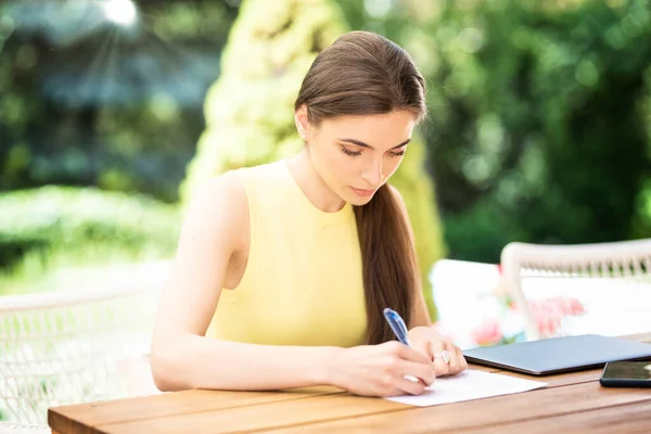 庭の机に座って試験のために勉強する美しい若い女性のショット — ストック写真
