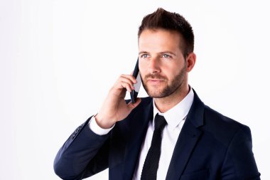 Yakından, beyaz arka planda dikilip cep telefonunu kullanan takım elbiseli yakışıklı bir adamın fotoğrafı. Boşluğu kopyala. 