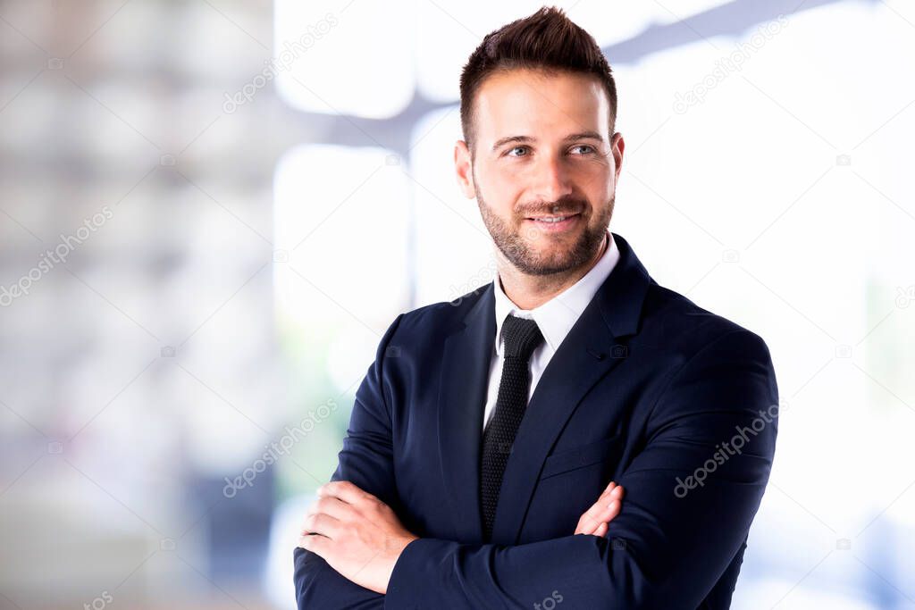 Portrait shot of handsome businessman standing with arms crossed in the office. 