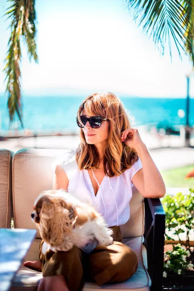 Orta yaşlı bir kadının güneşli bir günün tadını çıkarırken kral Charles Cavalier köpeğiyle deniz kenarında dinlenirken çekilmesi.. 